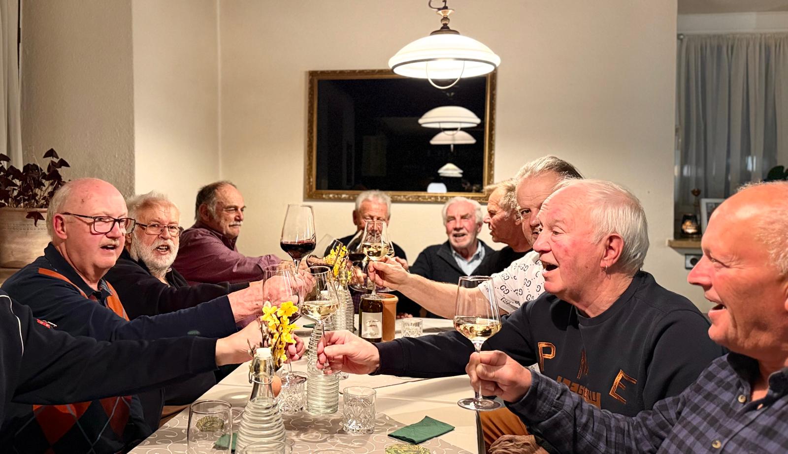 Ältere Männer stoßen gemeinsam mit Wein an.